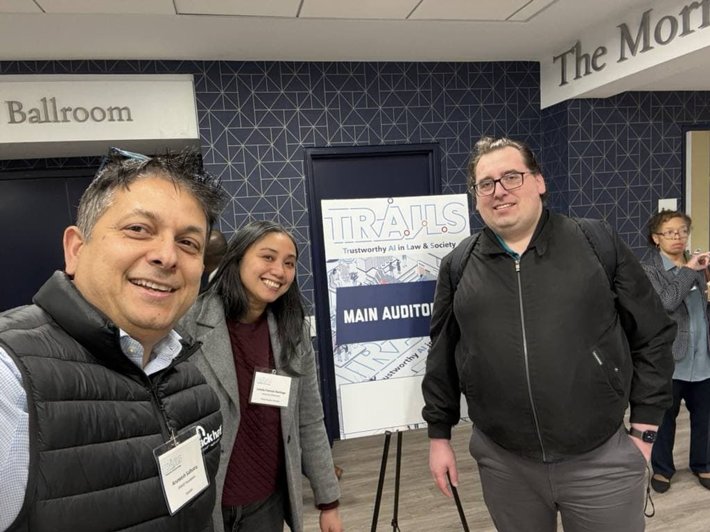 Aruneesh Salhotra with colleagues by the TRAILSCon 2026 main auditorium sign